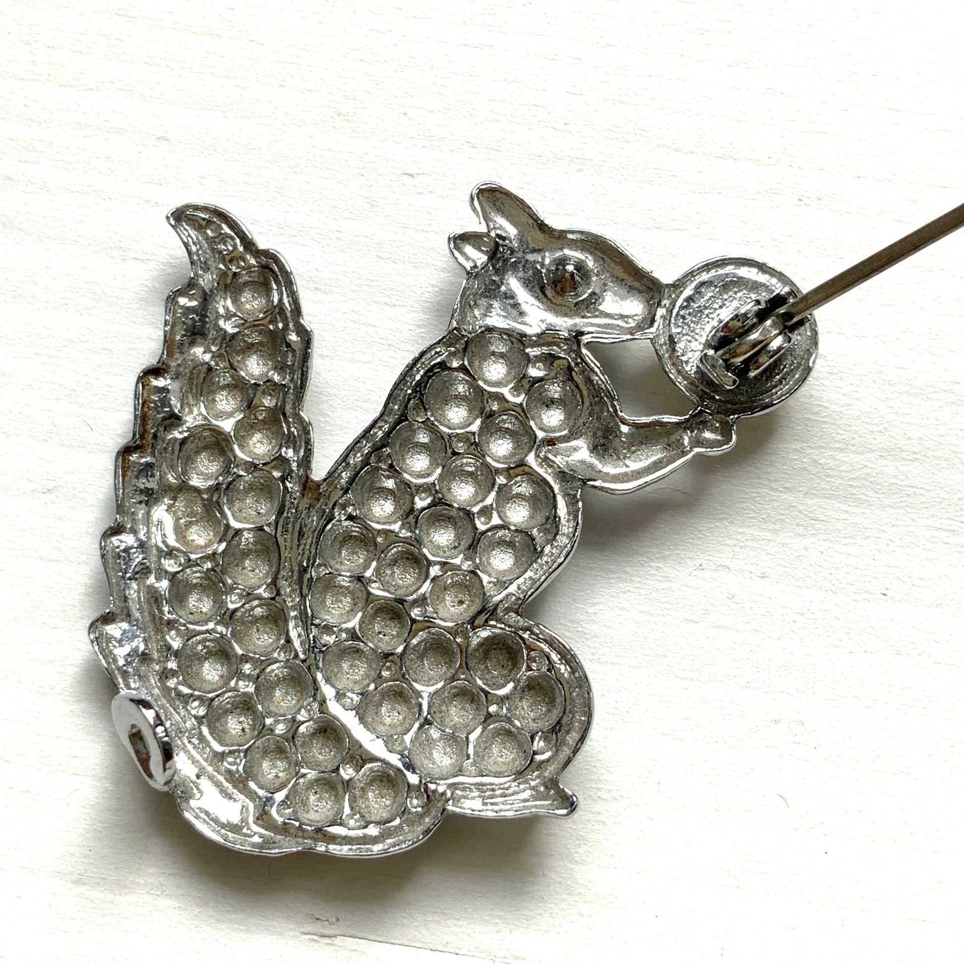 A silver-tone squirrel brooch holding a faux pearl acorn. シルバートーンのきらめくボディに、フェイクパールの実を抱えたリスのブローチ。
