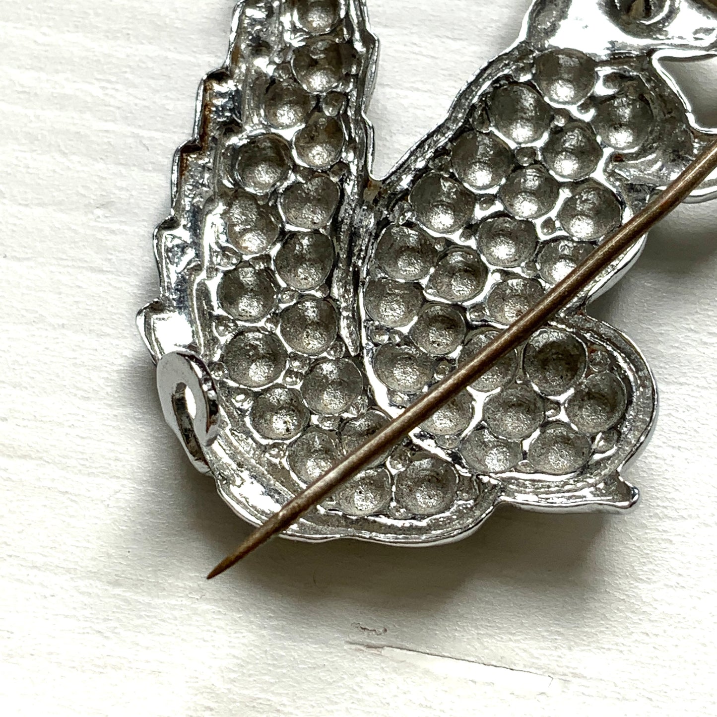 A silver-tone squirrel brooch holding a faux pearl acorn. シルバートーンのきらめくボディに、フェイクパールの実を抱えたリスのブローチ。