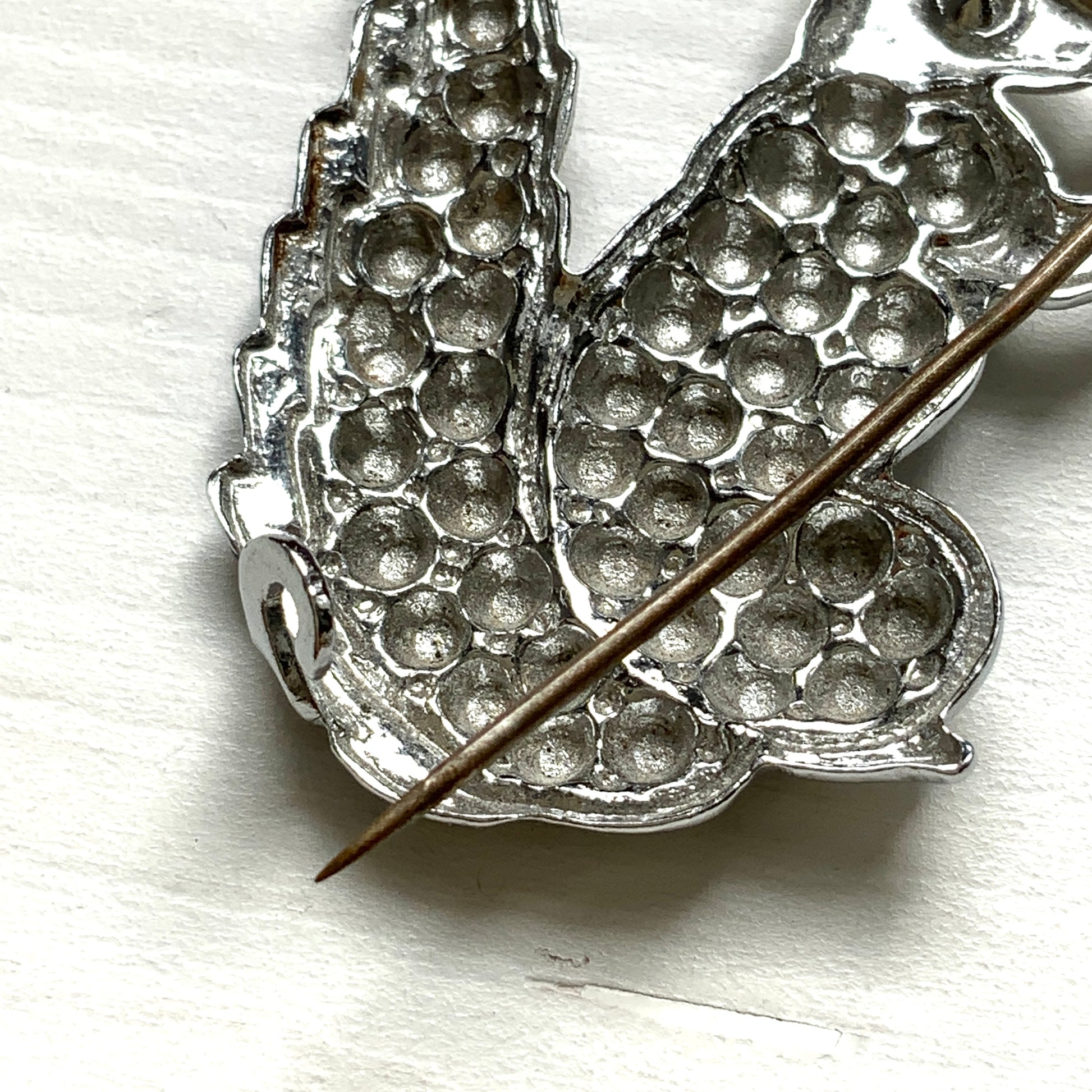 A silver-tone squirrel brooch holding a faux pearl acorn. シルバートーンのきらめくボディに、フェイクパールの実を抱えたリスのブローチ。