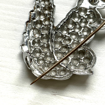 A silver-tone squirrel brooch holding a faux pearl acorn. シルバートーンのきらめくボディに、フェイクパールの実を抱えたリスのブローチ。