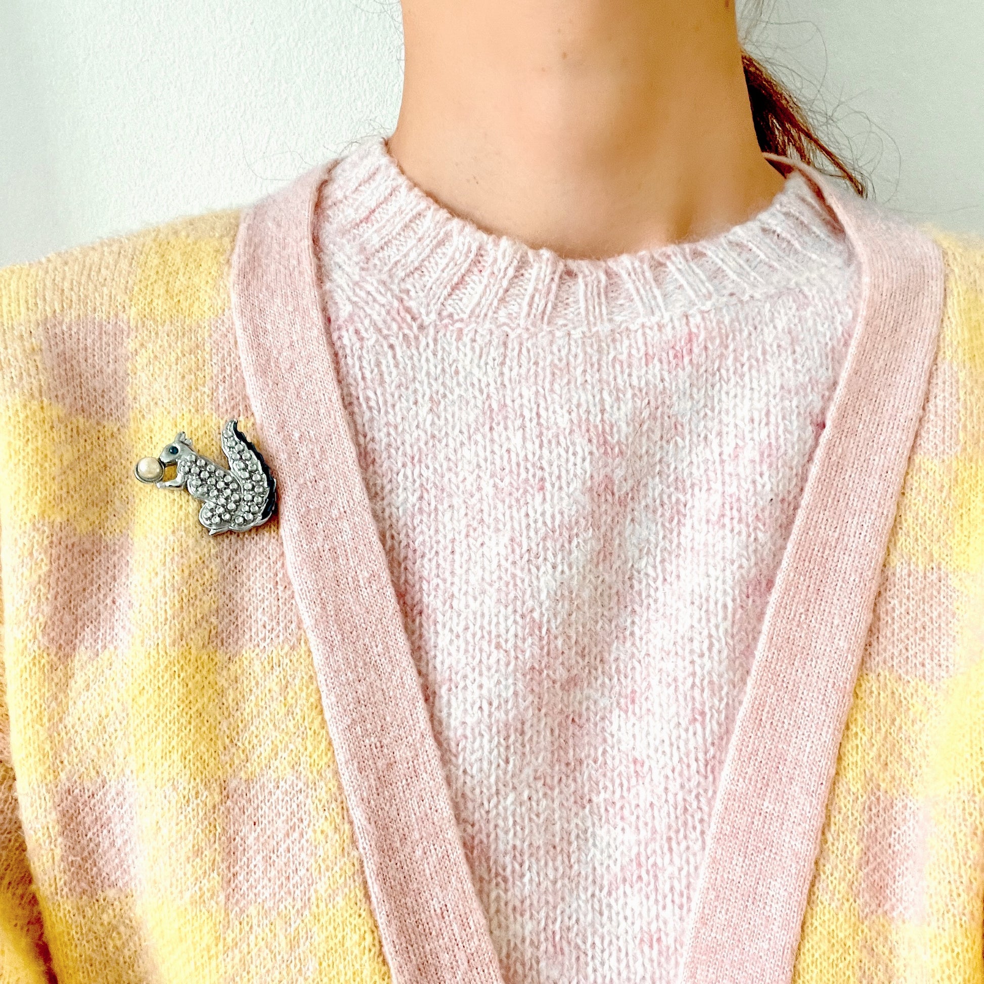 A silver-tone squirrel brooch holding a faux pearl acorn. シルバートーンのきらめくボディに、フェイクパールの実を抱えたリスのブローチ。