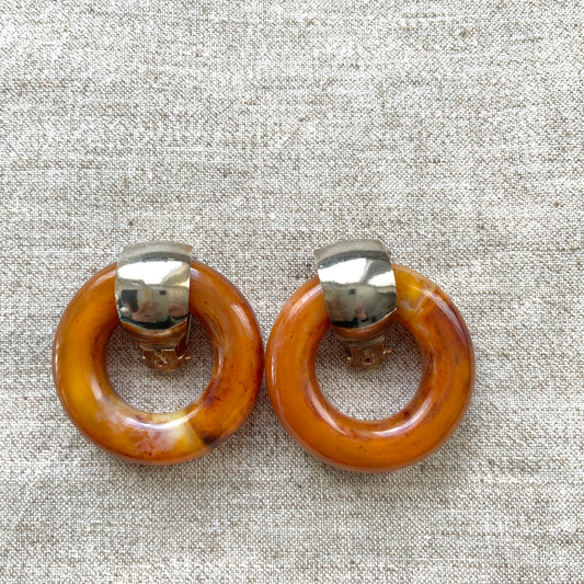 Clip-on door knocker earrings featuring amber-coloured plastic hoops. アンバーカラーのプラスチックフープが揺れる、ドアノッカータイプのクリップイヤリング。
