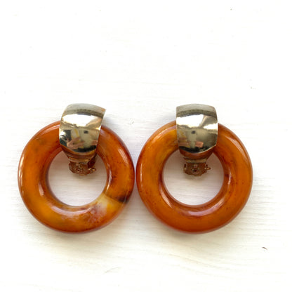Clip-on door knocker earrings featuring amber-coloured plastic hoops. アンバーカラーのプラスチックフープが揺れる、ドアノッカータイプのクリップイヤリング。