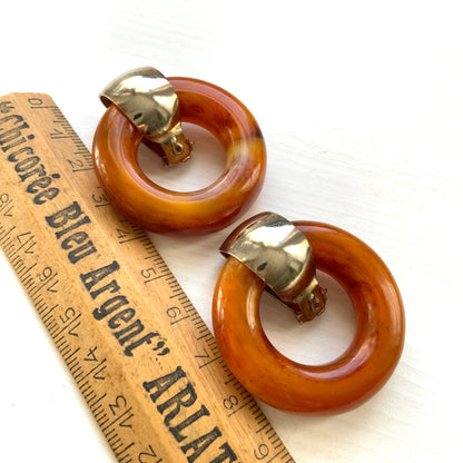 Clip-on door knocker earrings featuring amber-coloured plastic hoops. アンバーカラーのプラスチックフープが揺れる、ドアノッカータイプのクリップイヤリング。