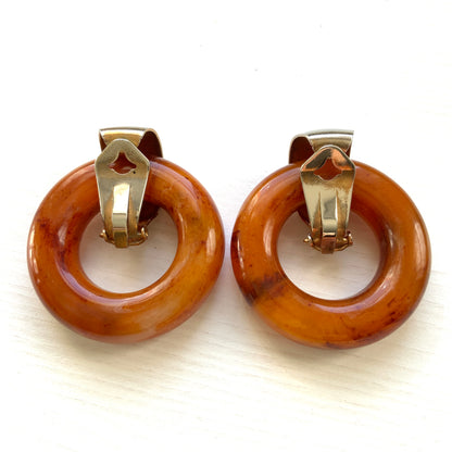Clip-on door knocker earrings featuring amber-coloured plastic hoops. アンバーカラーのプラスチックフープが揺れる、ドアノッカータイプのクリップイヤリング。
