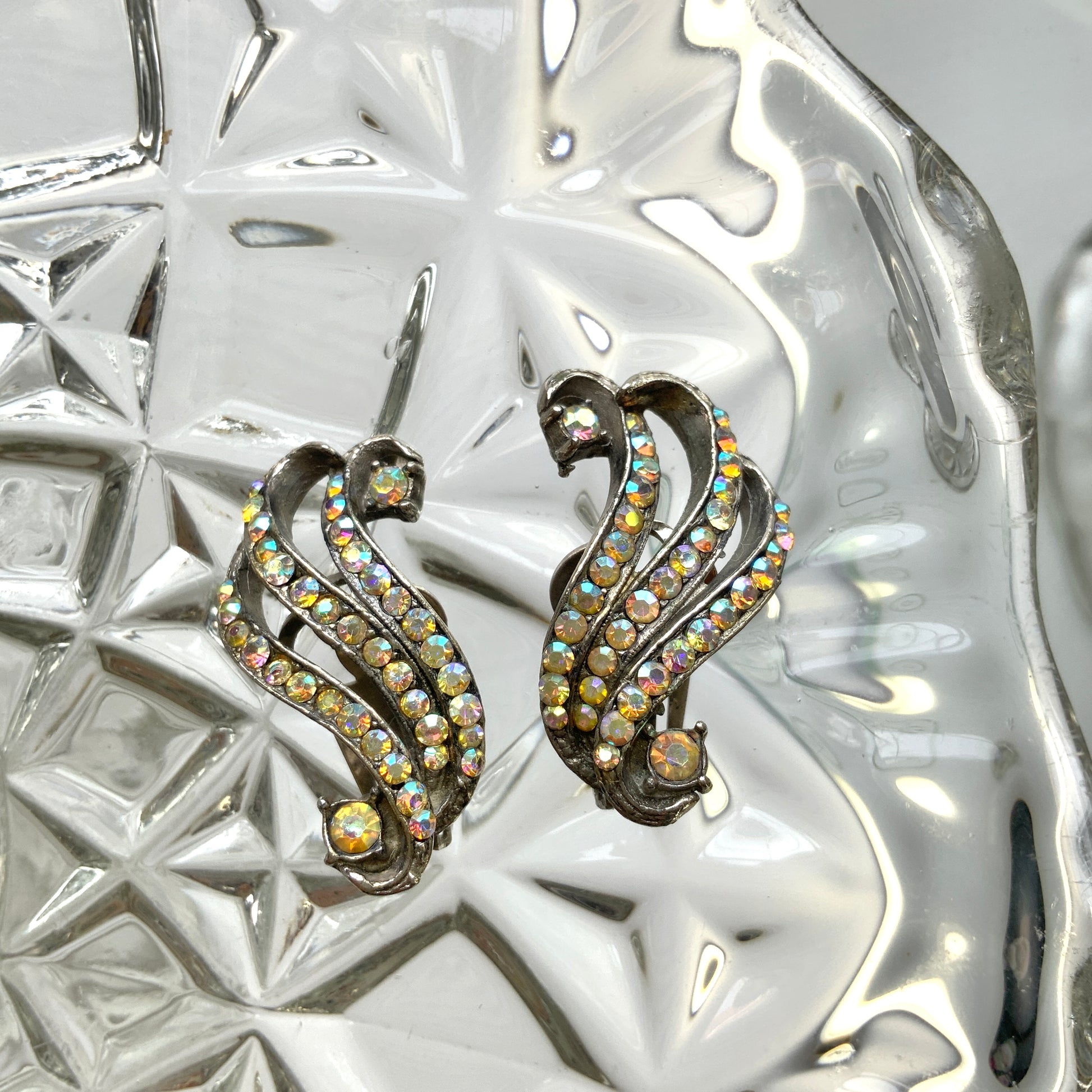 Clip-on earrings featuring aurora borealis rhinestones that trace a graceful curved line. 虹色に輝くオーロラストーンが緩やかなラインを描くクリップイヤリング。
