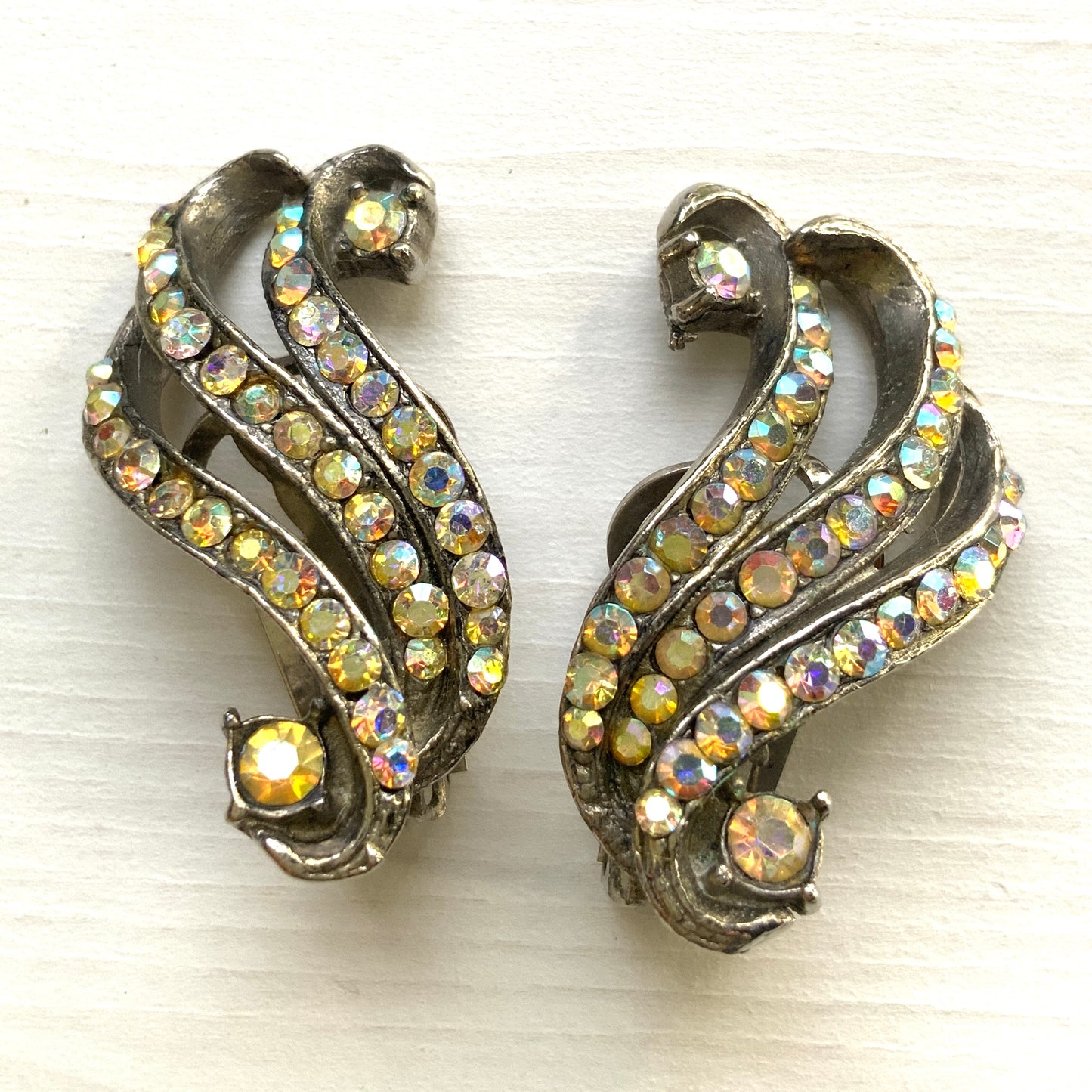Clip-on earrings featuring aurora borealis rhinestones that trace a graceful curved line. 虹色に輝くオーロラストーンが緩やかなラインを描くクリップイヤリング。