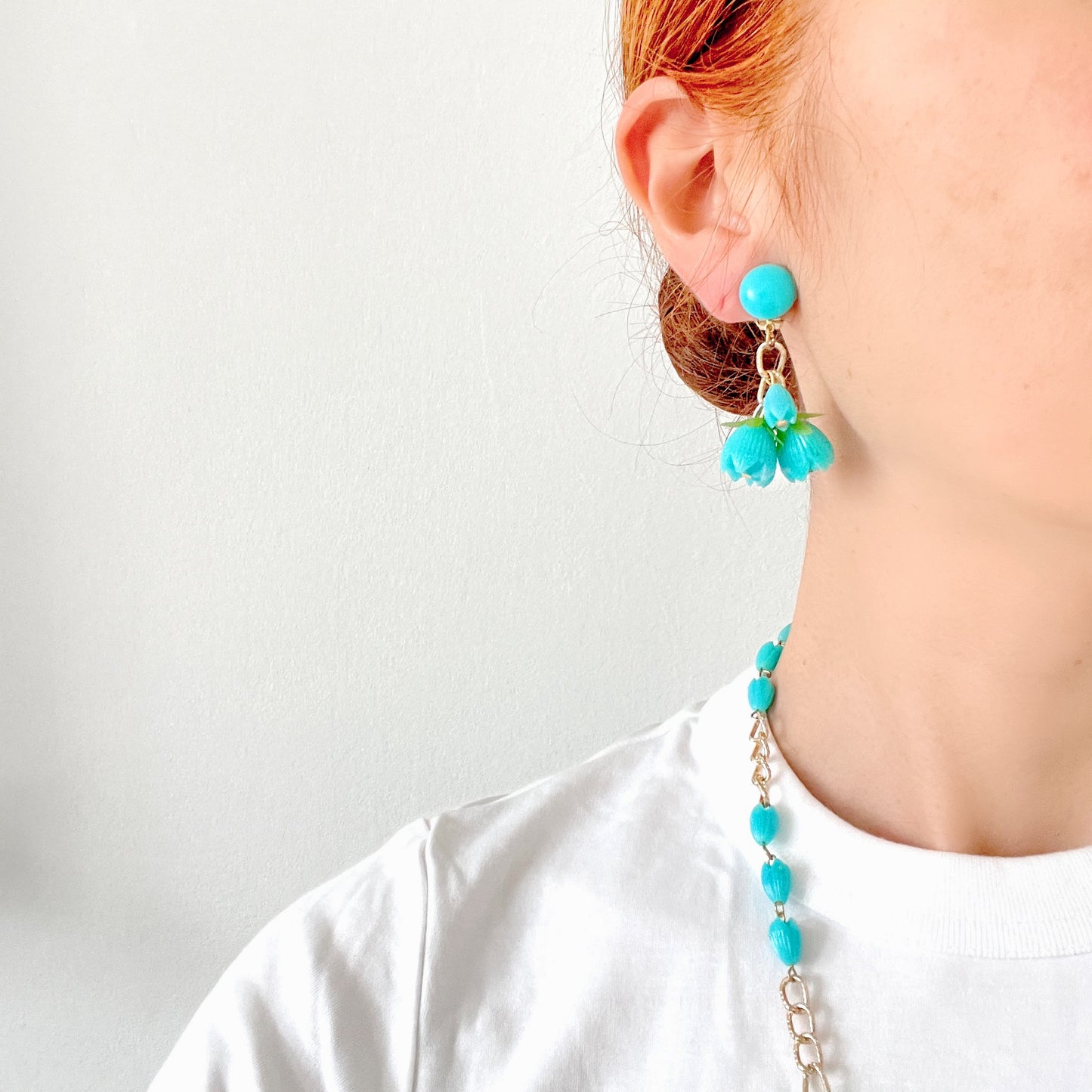 A pair of vintage clip-on earrings featuring dangling turquoise blue plastic flower beads. ターコイズブルーのプラスチックフラワービーズが揺れるヴィンテージクリップイヤリング。