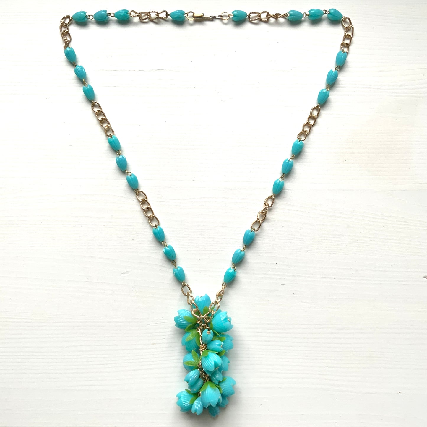 A vintage necklace featuring turquoise blue plastic flower beads that sway beautifully at the neckline.  ターコイズブルーのプラスチックフラワービーズが胸元で揺れるヴィンテージネックレス。