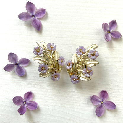 Charming clip-on earrings with pale purple blossoms adorning white enameled leaves. 白いエナメルの葉っぱに、かわいらしい薄紫のお花が咲いたクリップイヤリング。 