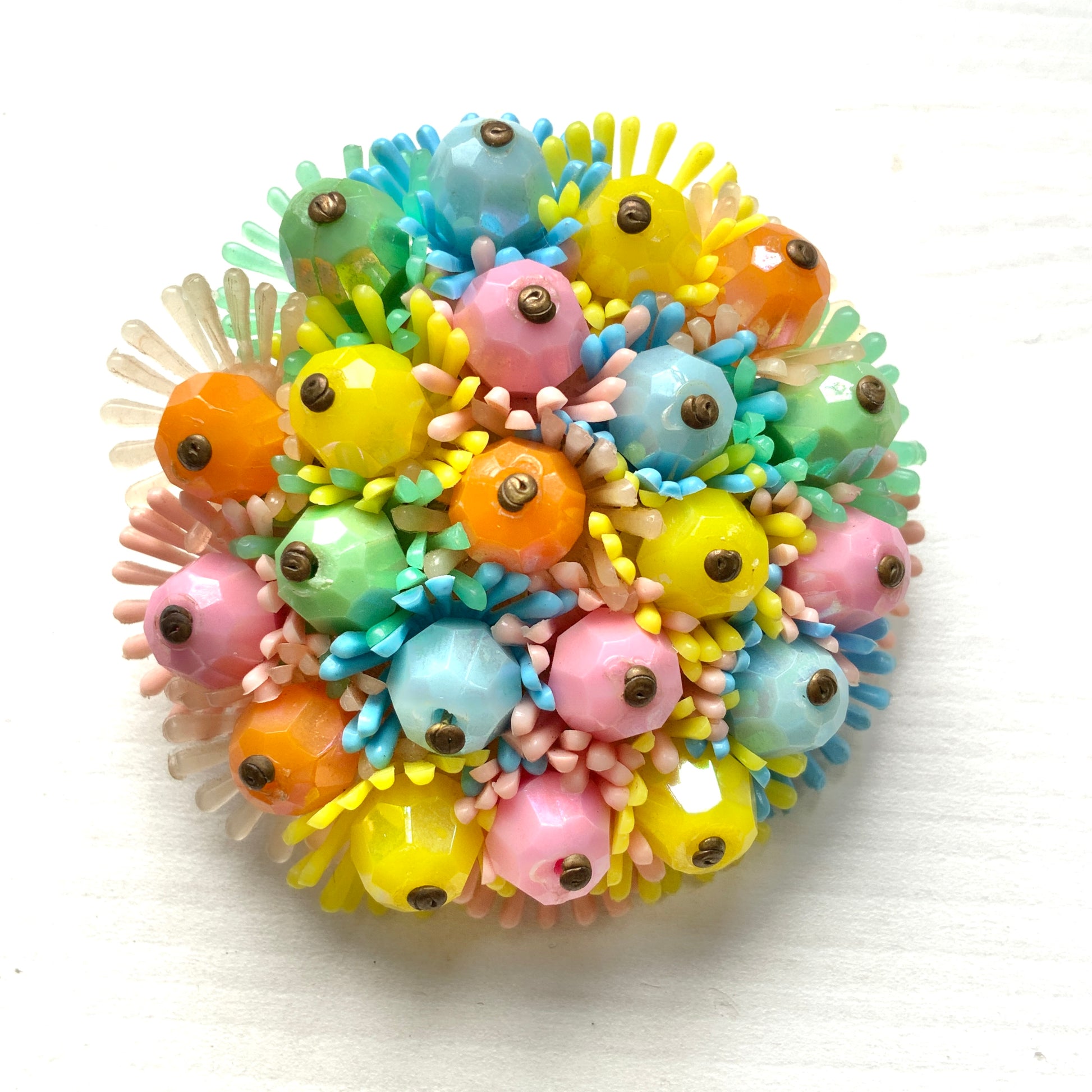 A round brooch featuring colourful candy-coloured soft plastic flowers. カラフルなキャンディーカラーのソフトプラスチックのお花が集まったラウンドブローチ。