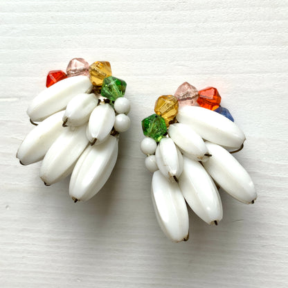 Clip-on earrings featuring layered white plastic beads arranged in a wing-like shape, accented with colourful faceted glass beads.  白い羽のようなロングプラスチックビーズに、カラフルなグラスビーズが彩りを添えたクリップイヤリング。