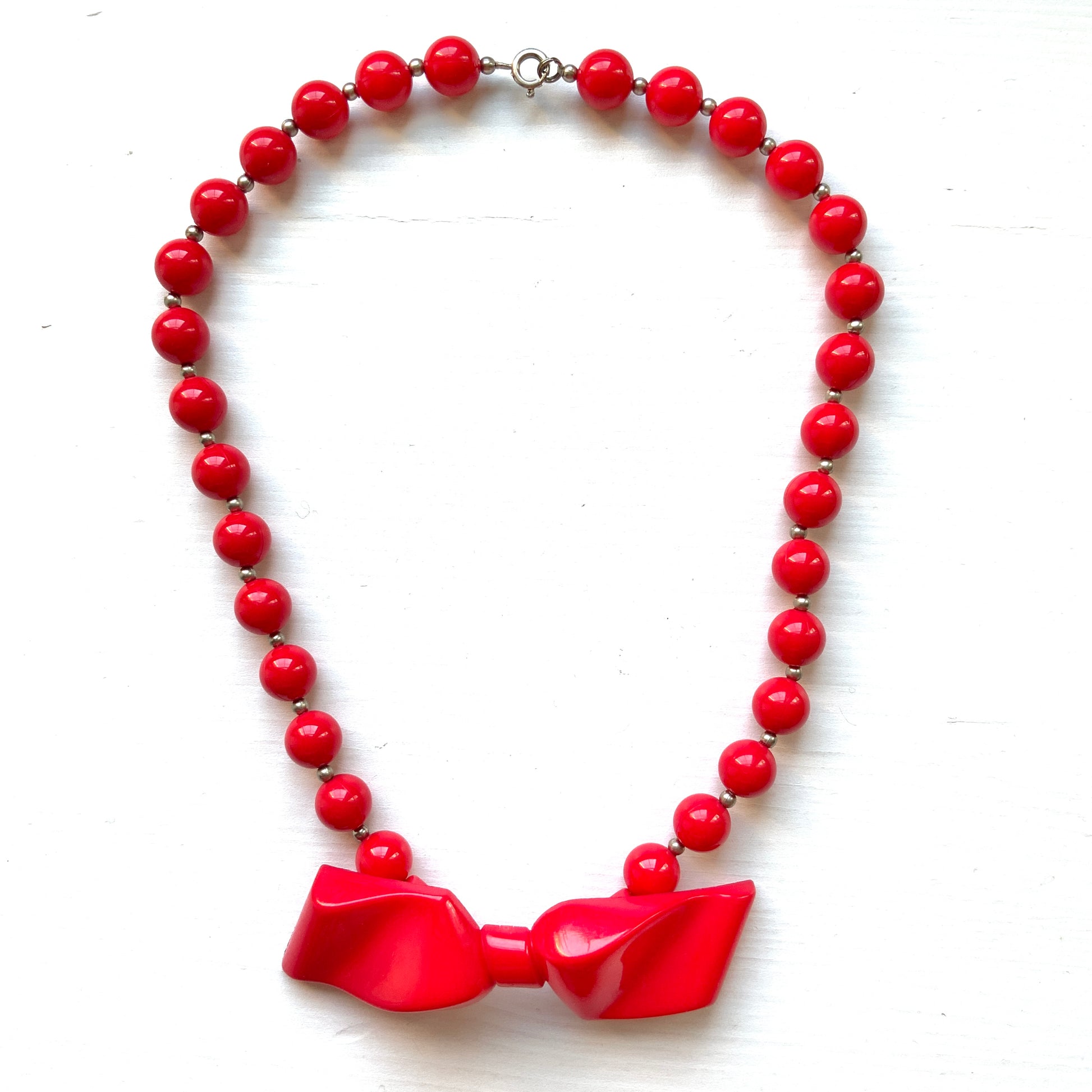 Vintage necklace featuring bright red plastic beads and a bow motif. 鮮やかなプラスチックのレッドビーズとリボンモチーフのネックレス。
