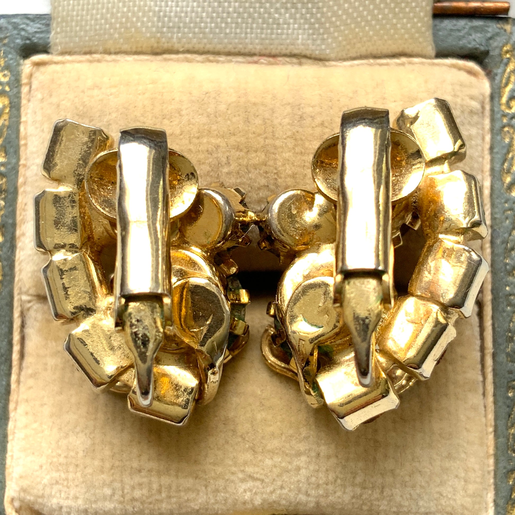 Clip-on earrings featuring vibrant orange and amber rhinestones, adorned with a petite beige enamel flower.  小さなベージュのエナメルフラワーが咲いた、アンバーラインストーンのクリップイヤリング。