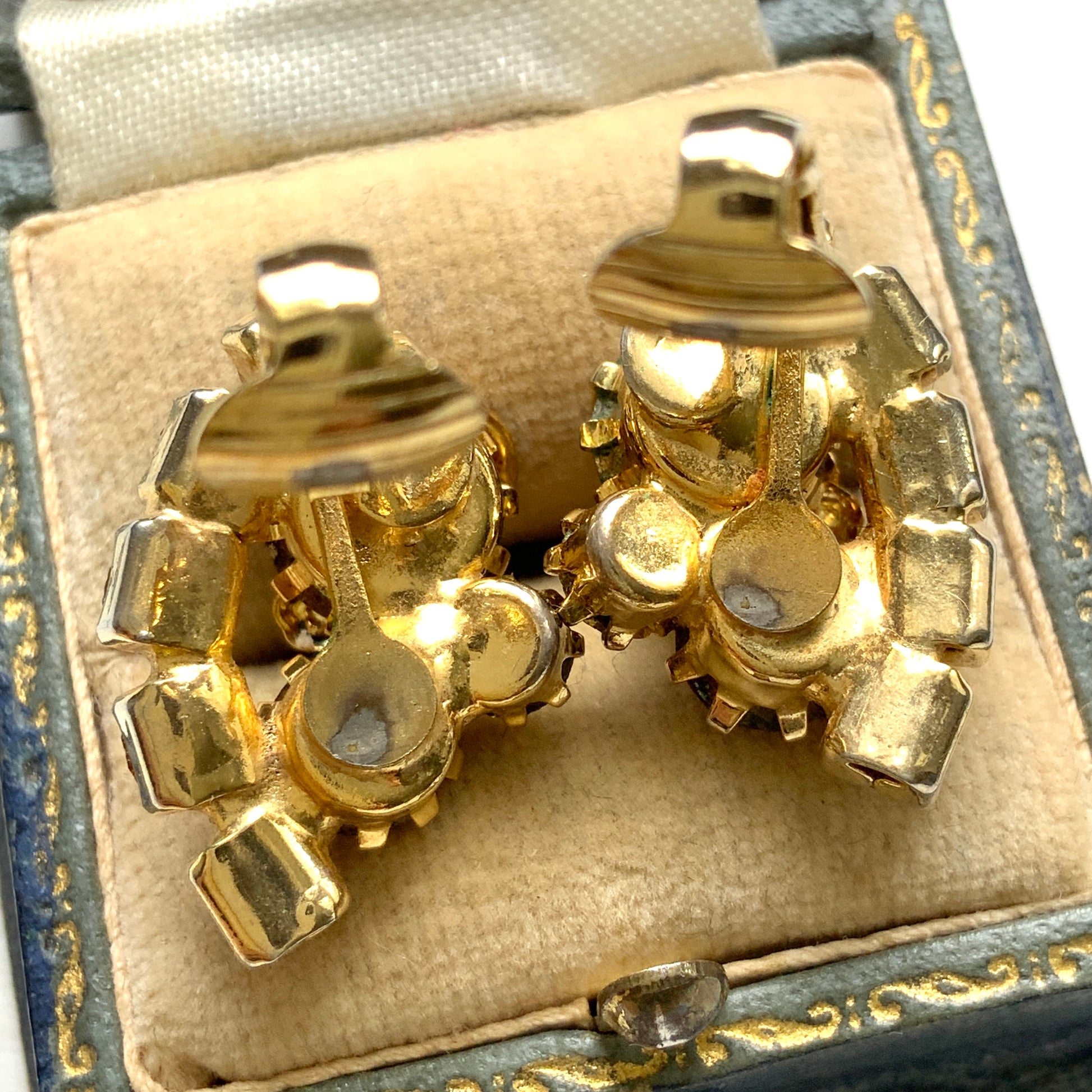 Clip-on earrings featuring vibrant orange and amber rhinestones, adorned with a petite beige enamel flower.  小さなベージュのエナメルフラワーが咲いた、アンバーラインストーンのクリップイヤリング。