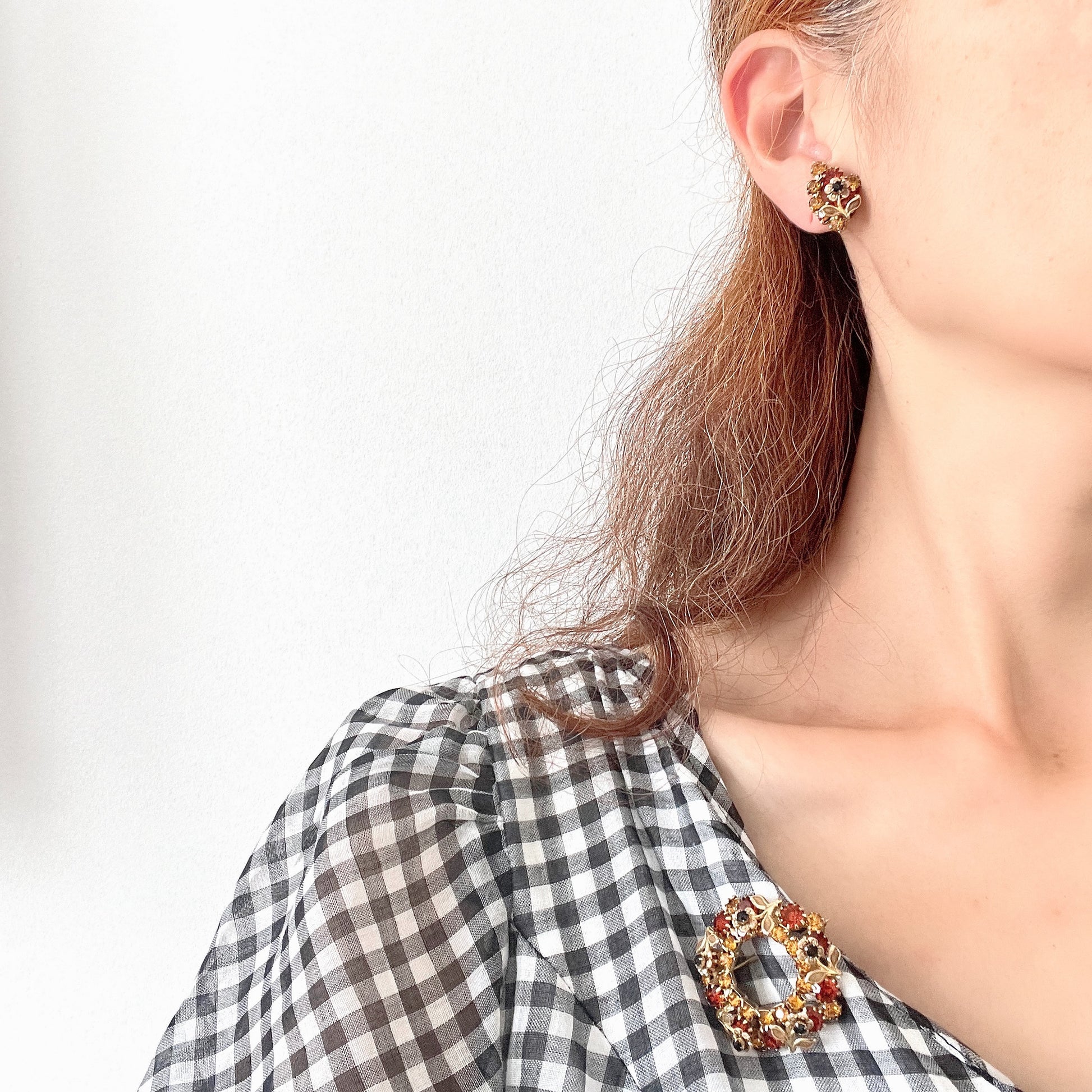 Clip-on earrings featuring vibrant orange and amber rhinestones, adorned with a petite beige enamel flower.  小さなベージュのエナメルフラワーが咲いた、アンバーラインストーンのクリップイヤリング。