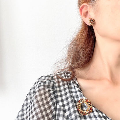 Clip-on earrings featuring vibrant orange and amber rhinestones, adorned with a petite beige enamel flower.  小さなベージュのエナメルフラワーが咲いた、アンバーラインストーンのクリップイヤリング。