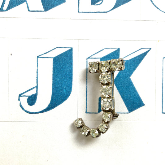 A brooch in the shape of the letter “J”, set with clear rhinestones. クリアラインストーンで”J”を象ったブローチ。