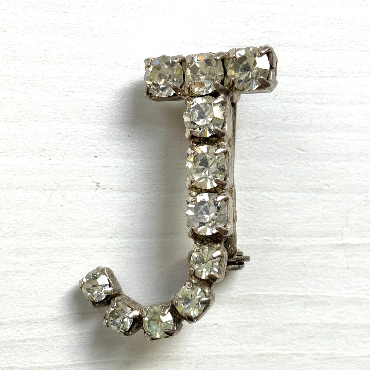 A brooch in the shape of the letter “J”, set with clear rhinestones. クリアラインストーンで”J”を象ったブローチ。