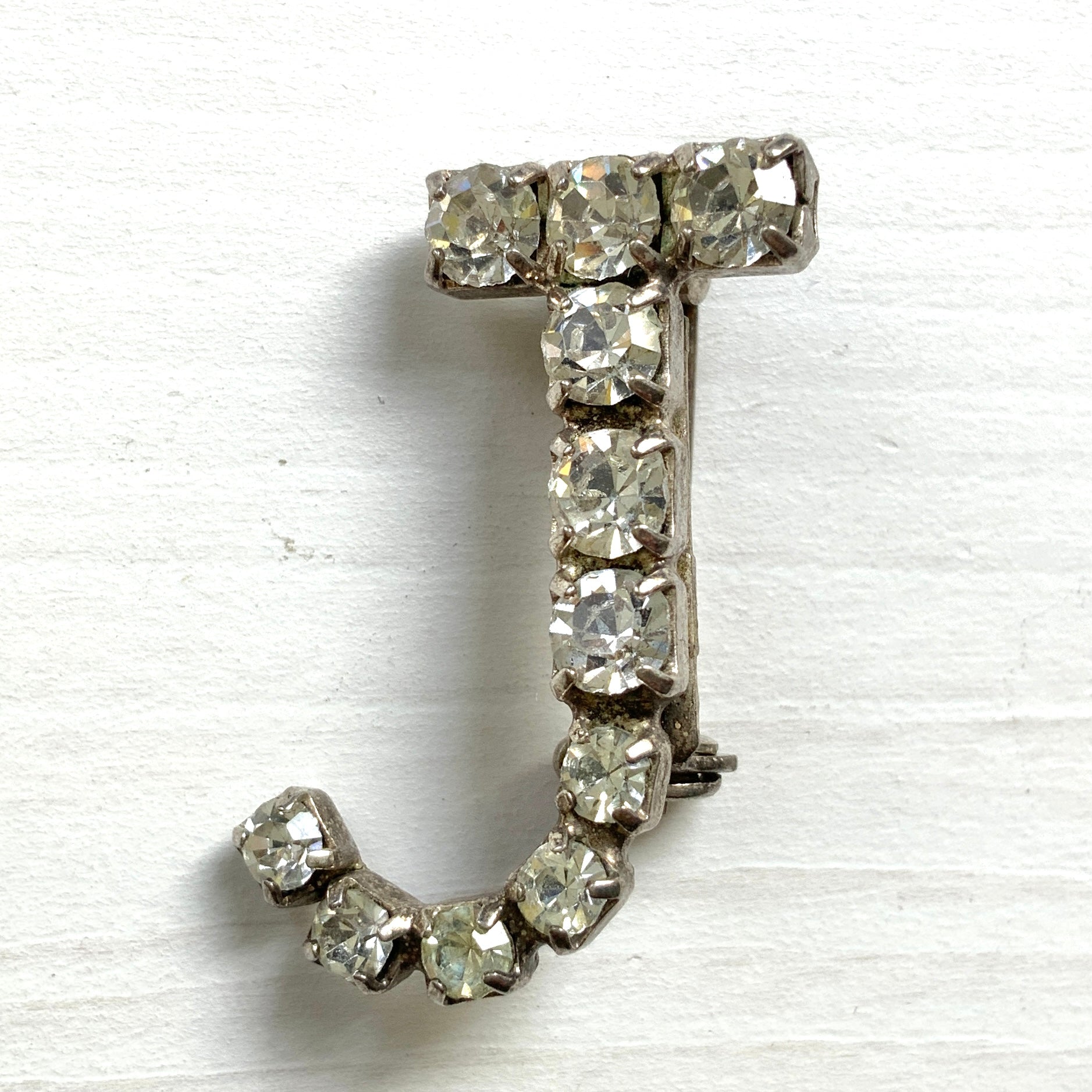 A brooch in the shape of the letter “J”, set with clear rhinestones. クリアラインストーンで”J”を象ったブローチ。