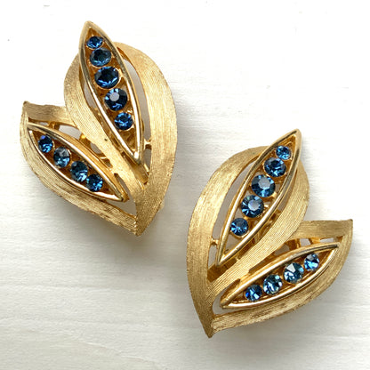 Trifari clip-on earrings featuring slim, bamboo leaf–like gold-tone leaves adorned with a row of blue rhinestones. 笹の葉のようにスリムなゴールドトーンのリーフに、ブルーのラインストーンが並んだトリファリのイヤリング。 