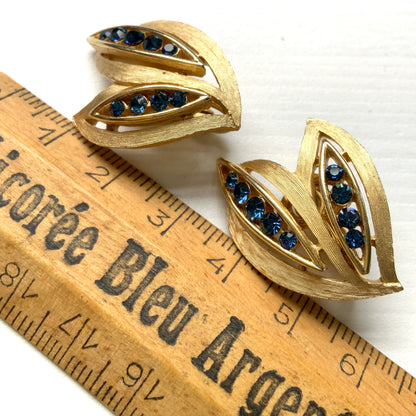 Trifari clip-on earrings featuring slim, bamboo leaf–like gold-tone leaves adorned with a row of blue rhinestones. 笹の葉のようにスリムなゴールドトーンのリーフに、ブルーのラインストーンが並んだトリファリのイヤリング。 