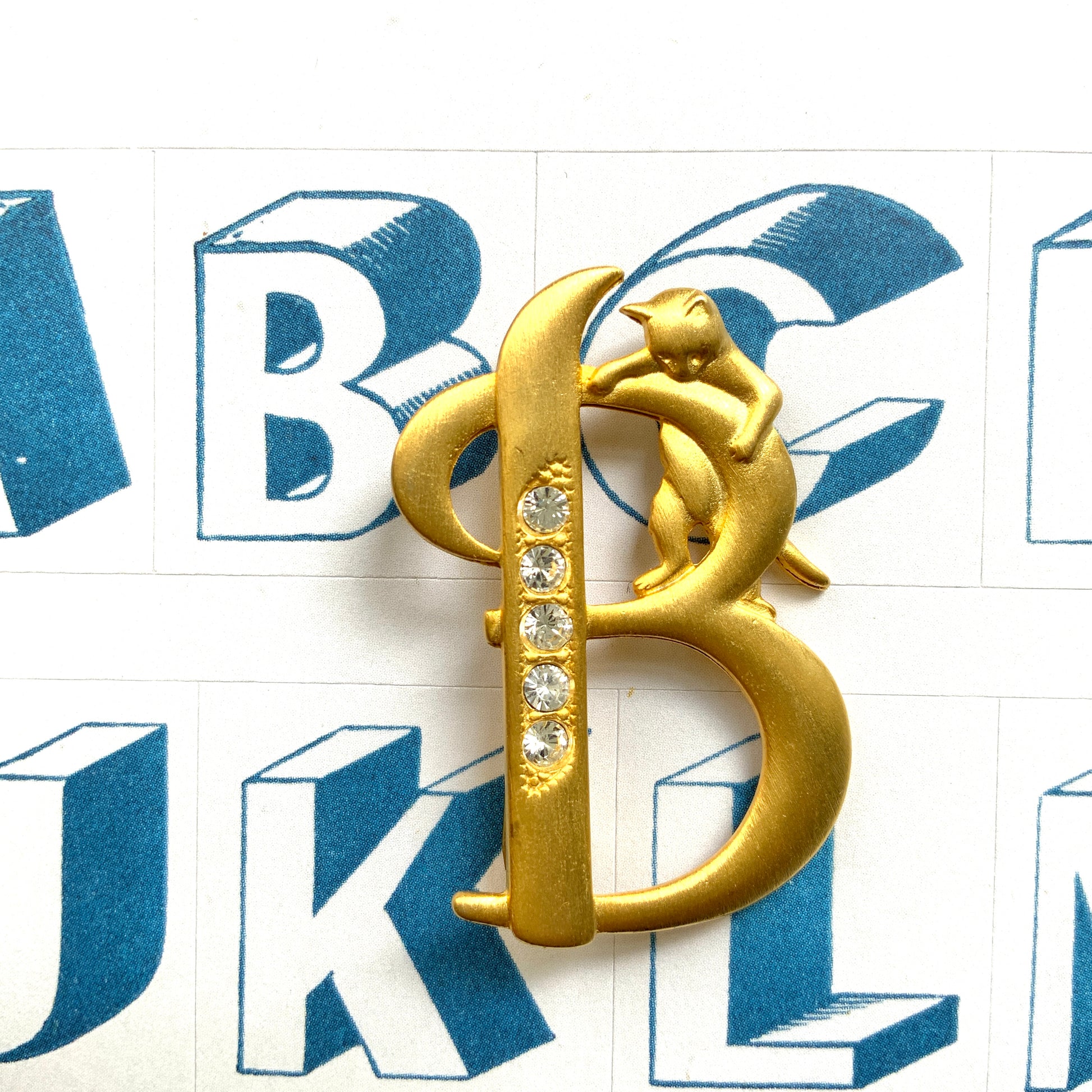 A gold-tone brooch in the shape of the letter “B”, with an adorable kitten clinging to it. かわいい子猫がつかまってる、ゴールドトーンのBのブローチ。