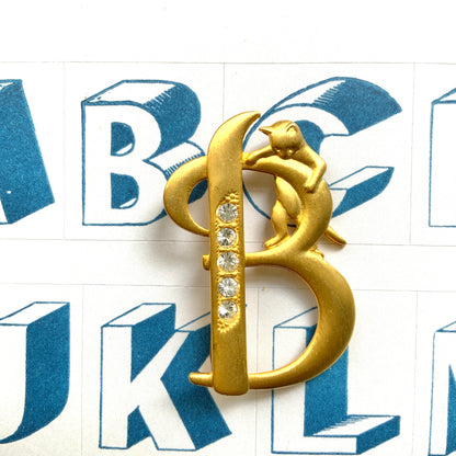 A gold-tone brooch in the shape of the letter “B”, with an adorable kitten clinging to it. かわいい子猫がつかまってる、ゴールドトーンのBのブローチ。