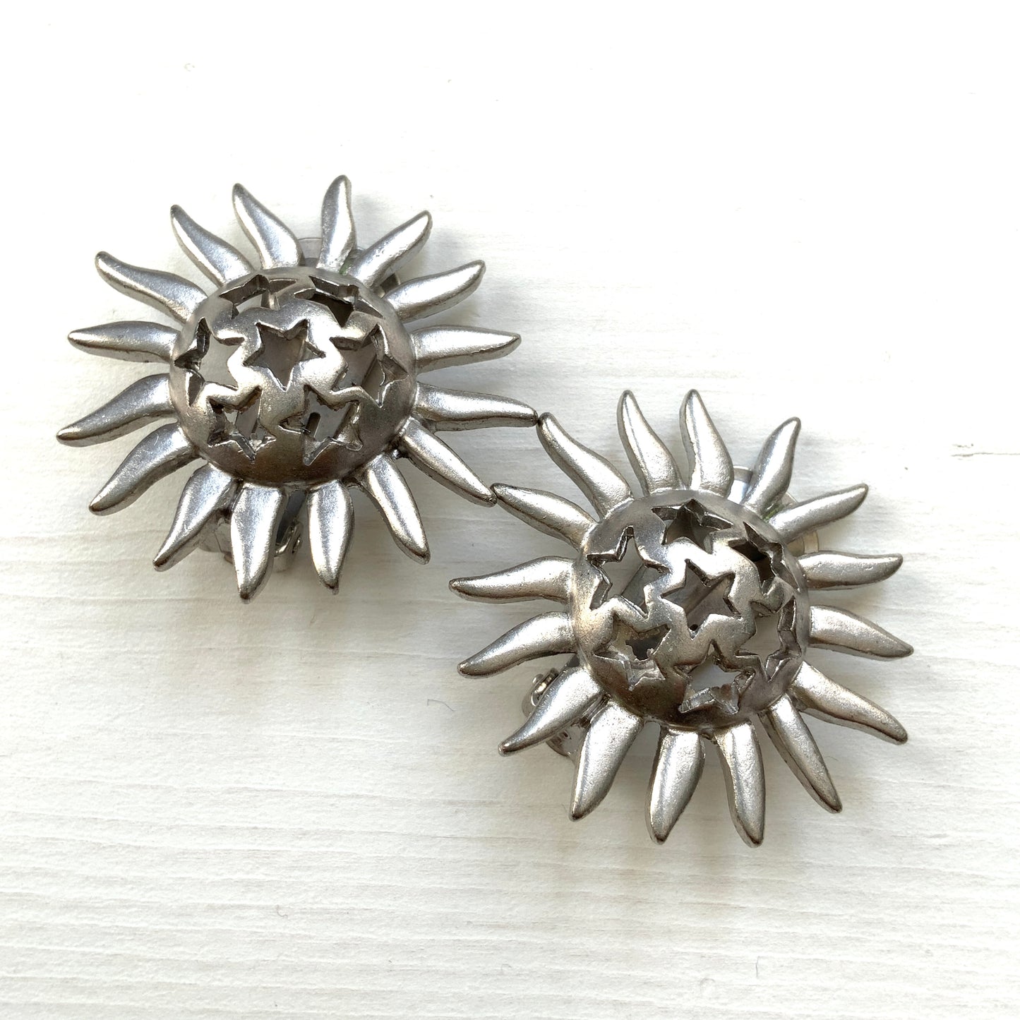 Clip-on earrings featuring a silver-tone sun motif with star-shaped cut-outs. シルバートーンの太陽モチーフに、星型のカットアウトが施されたクリップイヤリング。