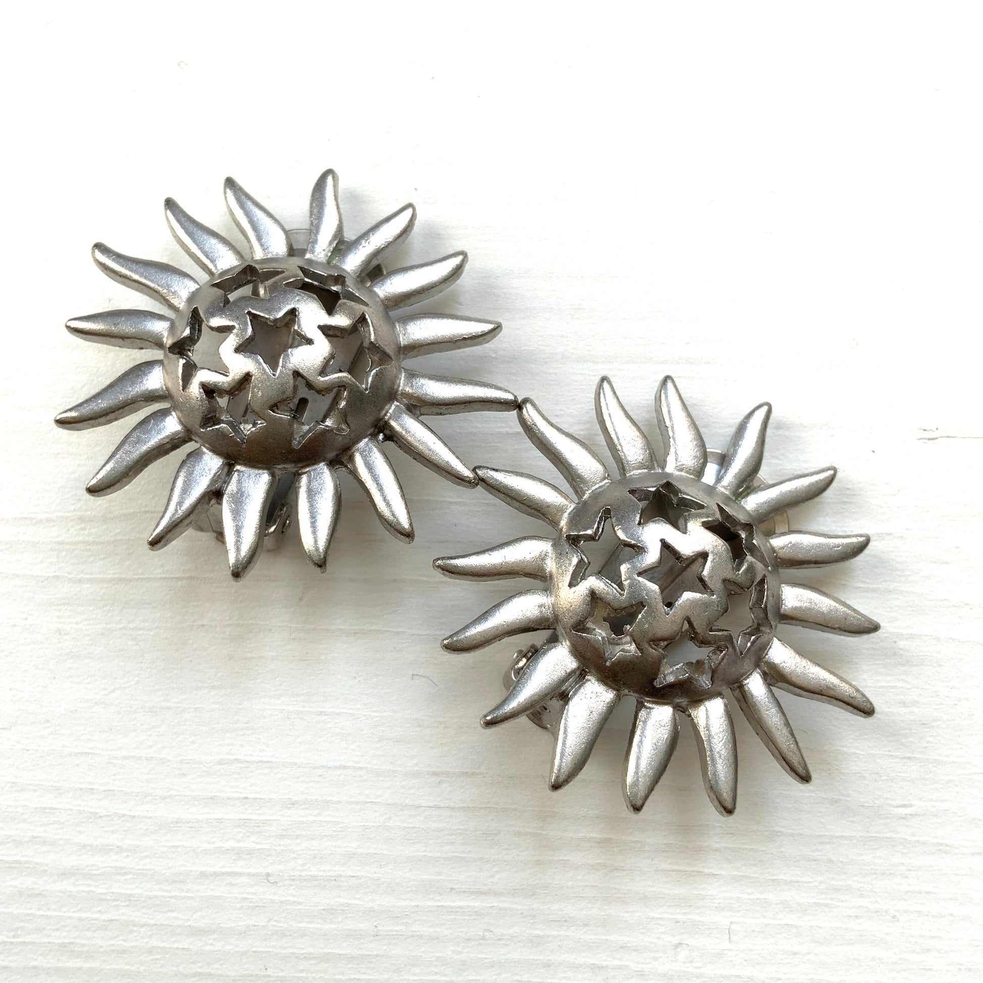 Clip-on earrings featuring a silver-tone sun motif with star-shaped cut-outs. シルバートーンの太陽モチーフに、星型のカットアウトが施されたクリップイヤリング。