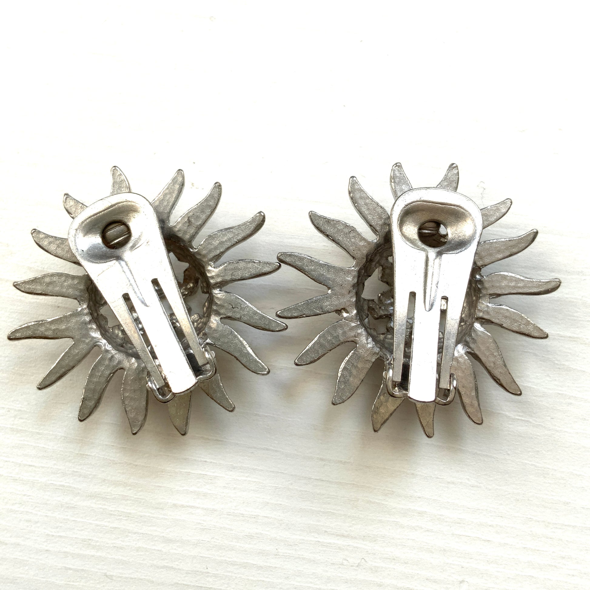 Clip-on earrings featuring a silver-tone sun motif with star-shaped cut-outs. シルバートーンの太陽モチーフに、星型のカットアウトが施されたクリップイヤリング。