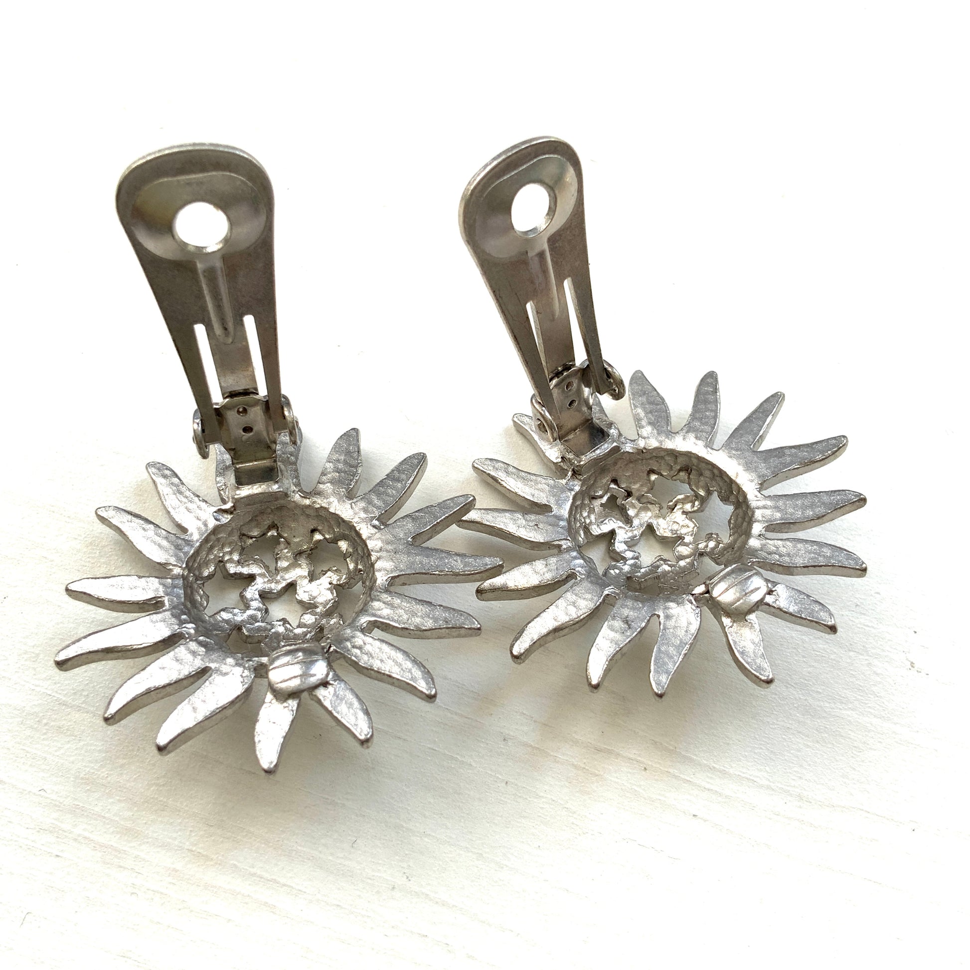 Clip-on earrings featuring a silver-tone sun motif with star-shaped cut-outs. シルバートーンの太陽モチーフに、星型のカットアウトが施されたクリップイヤリング。