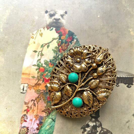 A gold-tone locket brooch featuring a floral motif accented with turquoise blue cabochons.  ゴールドトーンのお花に、ターコイズブルーのカボションが映えるロケットブローチ。
