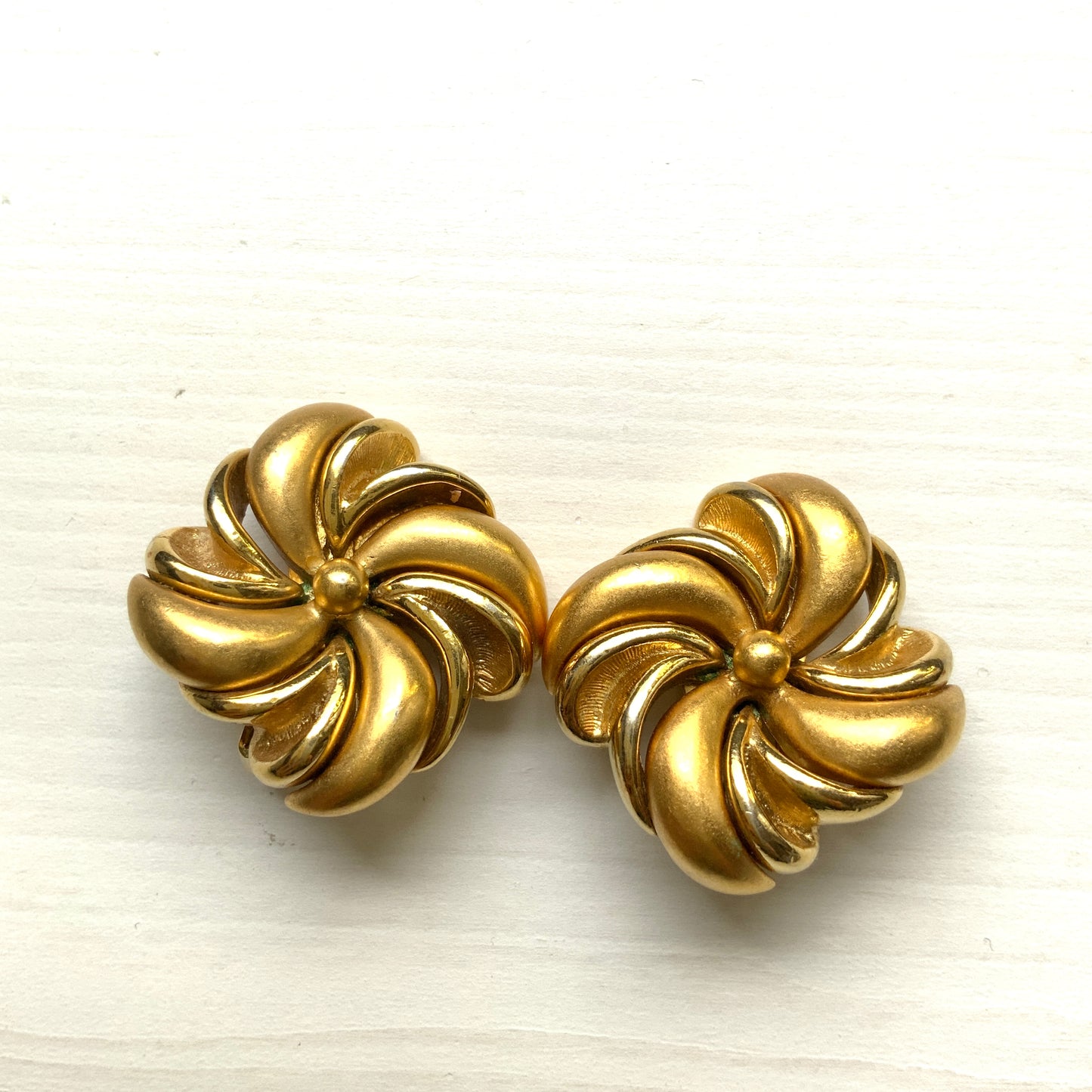 Gold-tone swirl clip-on earrings with curved, sculptural lines. 曲線的なスワールモチーフが印象的な、ゴールドトーンのクリップイヤリング。