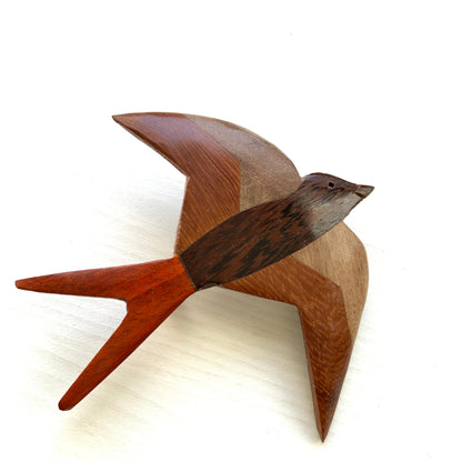 A wooden swallow brooch made from different shades of natural wood. 色味の異なる木材を組み合わせて作られた、ツバメモチーフのウッドブローチ。