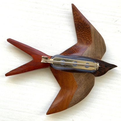 A wooden swallow brooch made from different shades of natural wood. 色味の異なる木材を組み合わせて作られた、ツバメモチーフのウッドブローチ。