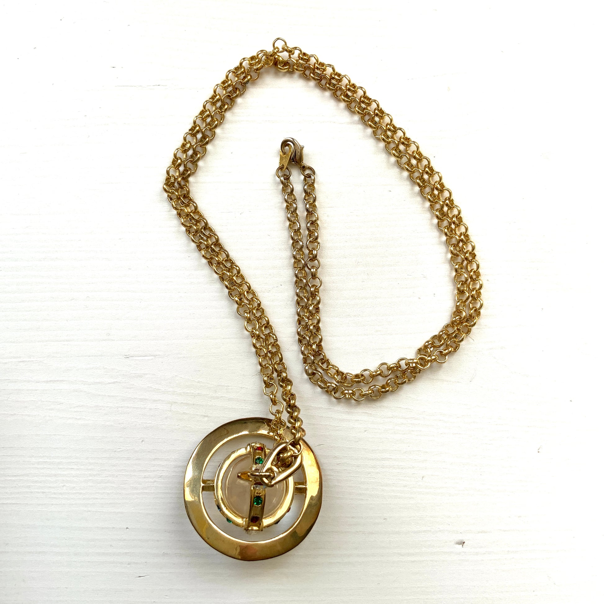 A striking pendant necklace featuring a decorative orb encircled by a metal hoop, resembling the rings of Saturn. カラフルなストーンで飾られた宝珠（キリスト教圏で、十字架をのせた球体として王権の象徴に用いられるモチーフ）を、まるで土星の輪のようなメタルフープで囲んだデザインのペンダントネックレスです。