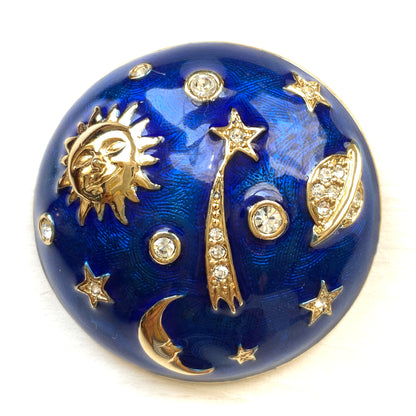 A dome-shaped brooch adorned with vibrant blue enamel, featuring silver-tone celestial motifs such as the sun face, crescent moon face, Saturn, and stars. 鮮やかなブルーのエナメルが施されたドームに、シルバートーンの太陽や三日月フェイスや、土星や星などが浮かんだブローチ。