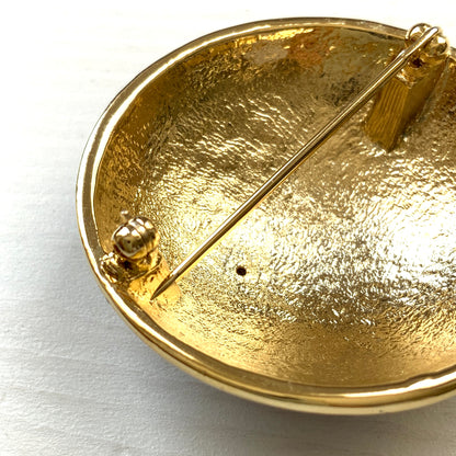 A dome-shaped brooch adorned with vibrant blue enamel, featuring silver-tone celestial motifs such as the sun face, crescent moon face, Saturn, and stars. 鮮やかなブルーのエナメルが施されたドームに、シルバートーンの太陽や三日月フェイスや、土星や星などが浮かんだブローチ。