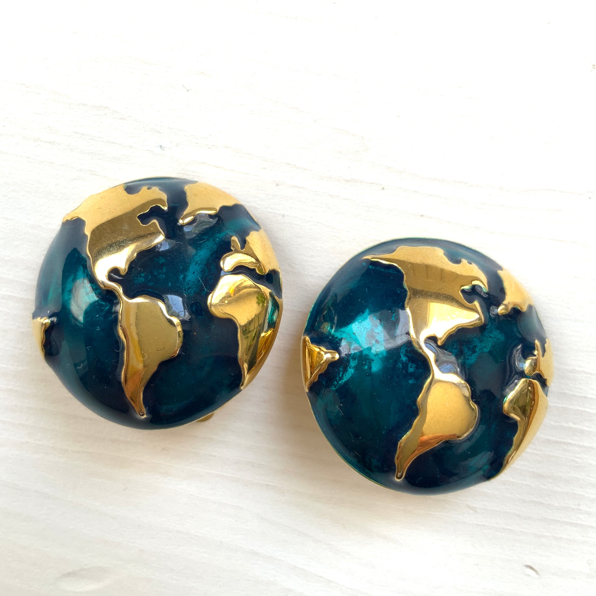 Clip-on earrings featuring a globe design with gold tone continents over a dome of deep ocean blue enamel.  深い海の色のエナメルドームにゴールドトーンで大陸をあしらった地球のクリップイヤリング。
