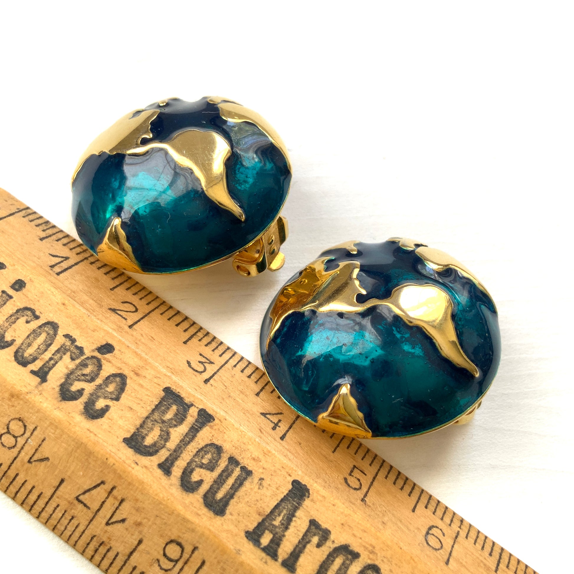 Clip-on earrings featuring a globe design with gold tone continents over a dome of deep ocean blue enamel.  深い海の色のエナメルドームにゴールドトーンで大陸をあしらった地球のクリップイヤリング。