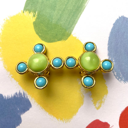 These clip-on earrings by Farah Lister feature a striking cross design with a refreshing apple green satin cabochon glass at the centre, paired with vivid turquoise glass stones. 爽やかなアップルグリーンのサテンカボショングラスとヴィヴィッドなターコイズグラスがクロスになった、ファラー・リスターのクリップイヤリング。 