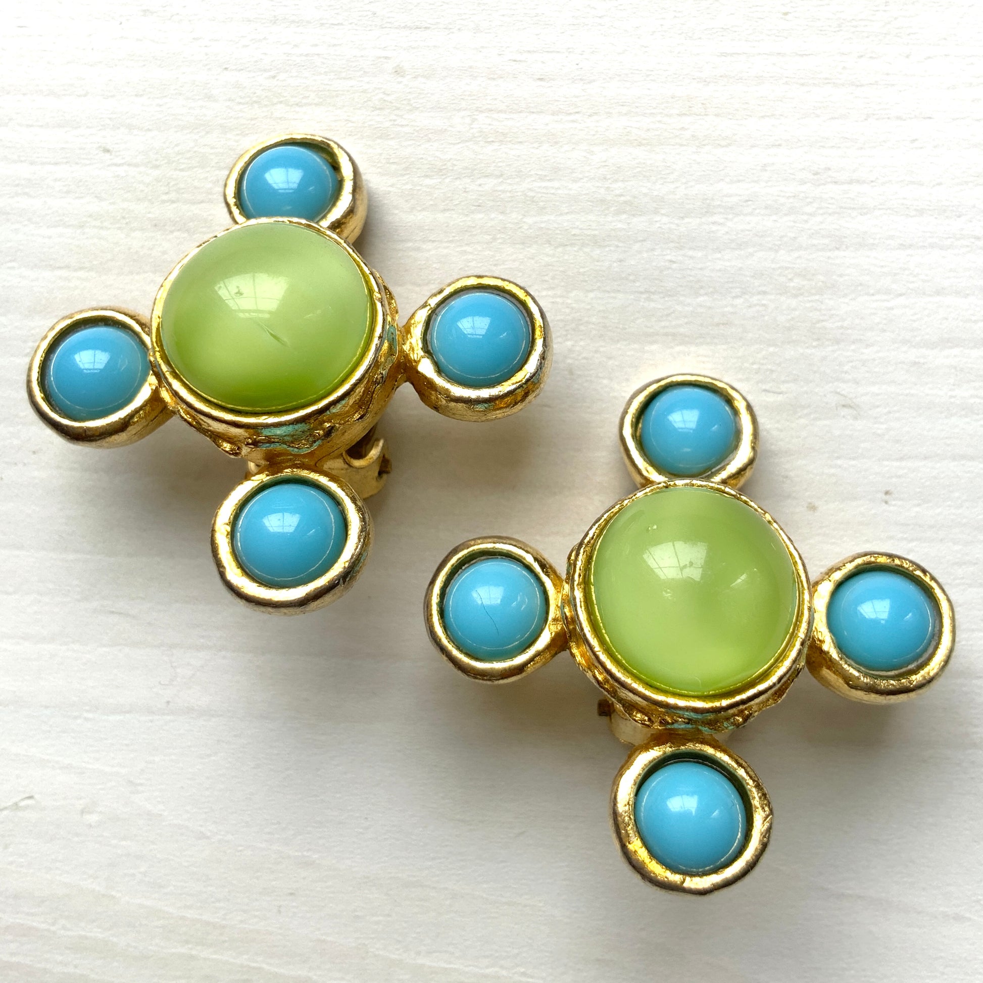These clip-on earrings by Farah Lister feature a striking cross design with a refreshing apple green satin cabochon glass at the centre, paired with vivid turquoise glass stones. 爽やかなアップルグリーンのサテンカボショングラスとヴィヴィッドなターコイズグラスがクロスになった、ファラー・リスターのクリップイヤリング。 