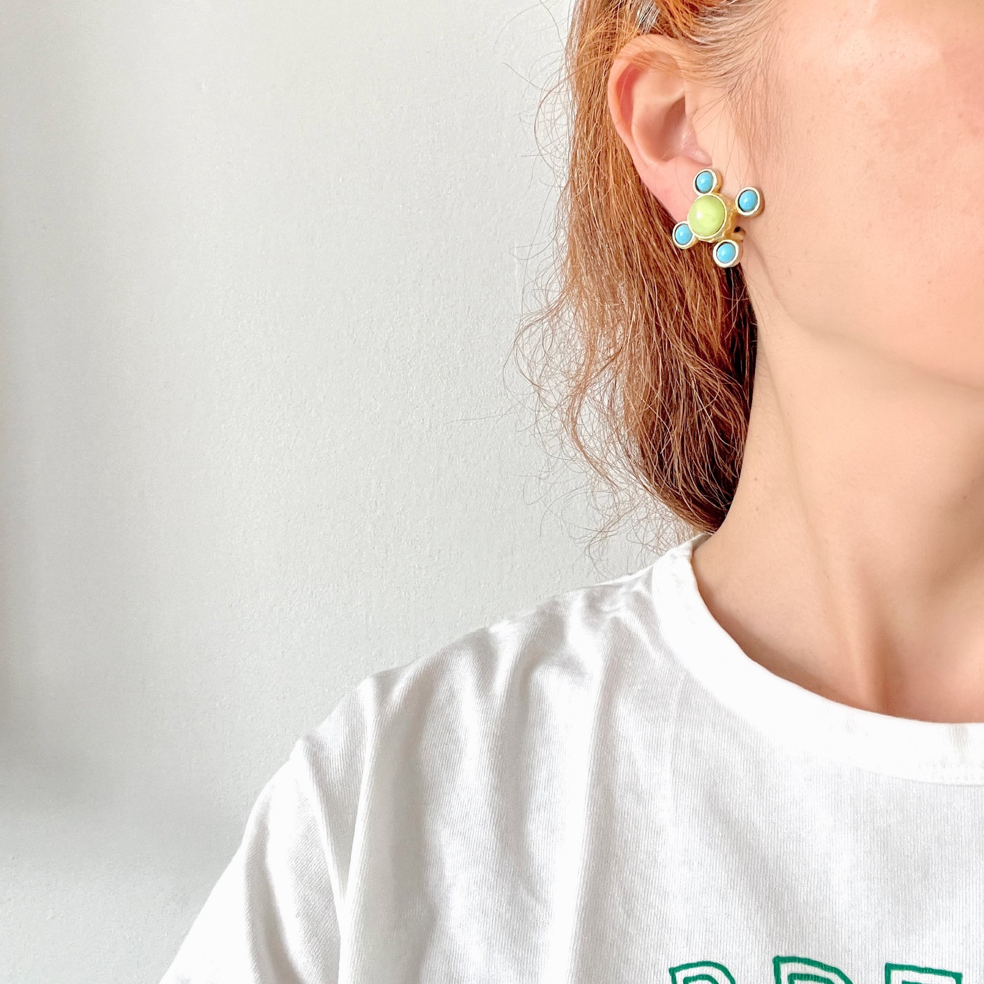 These clip-on earrings by Farah Lister feature a striking cross design with a refreshing apple green satin cabochon glass at the centre, paired with vivid turquoise glass stones. 爽やかなアップルグリーンのサテンカボショングラスとヴィヴィッドなターコイズグラスがクロスになった、ファラー・リスターのクリップイヤリング。 
