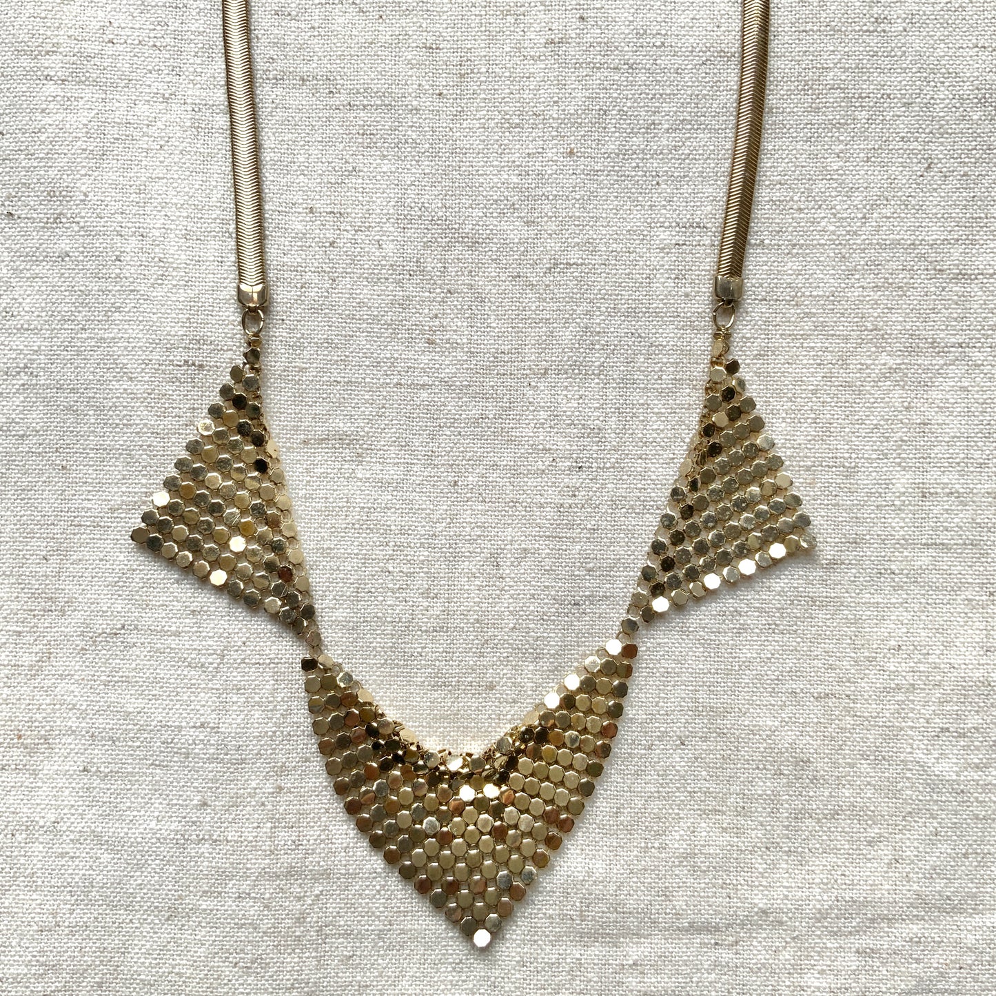 Gold-tone necklace featuring a combination of triangular metal mesh panels. 三角形のメタルメッシュを組み合わせた、ゴールドトーンのネックレス。