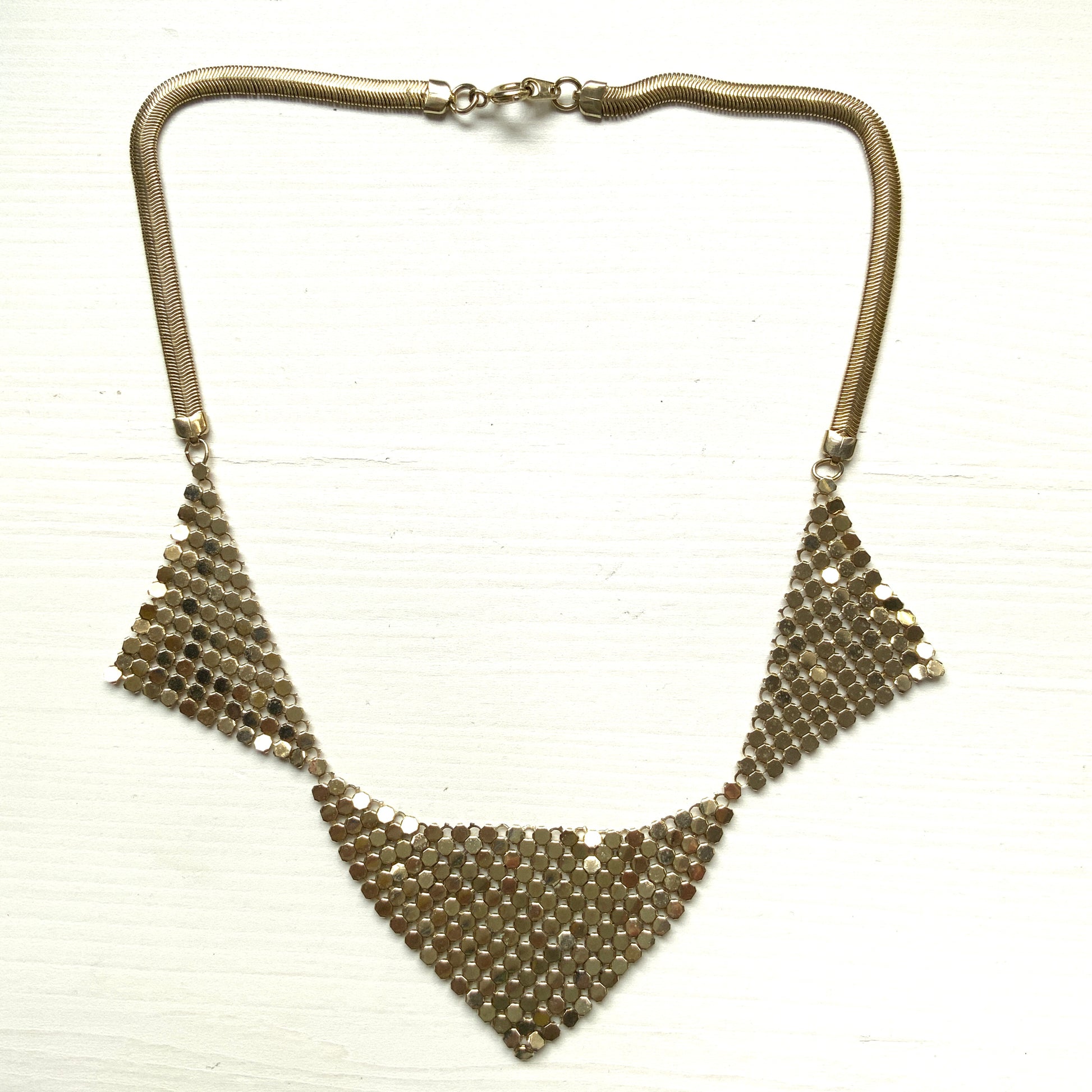 Gold-tone necklace featuring a combination of triangular metal mesh panels. 三角形のメタルメッシュを組み合わせた、ゴールドトーンのネックレス。