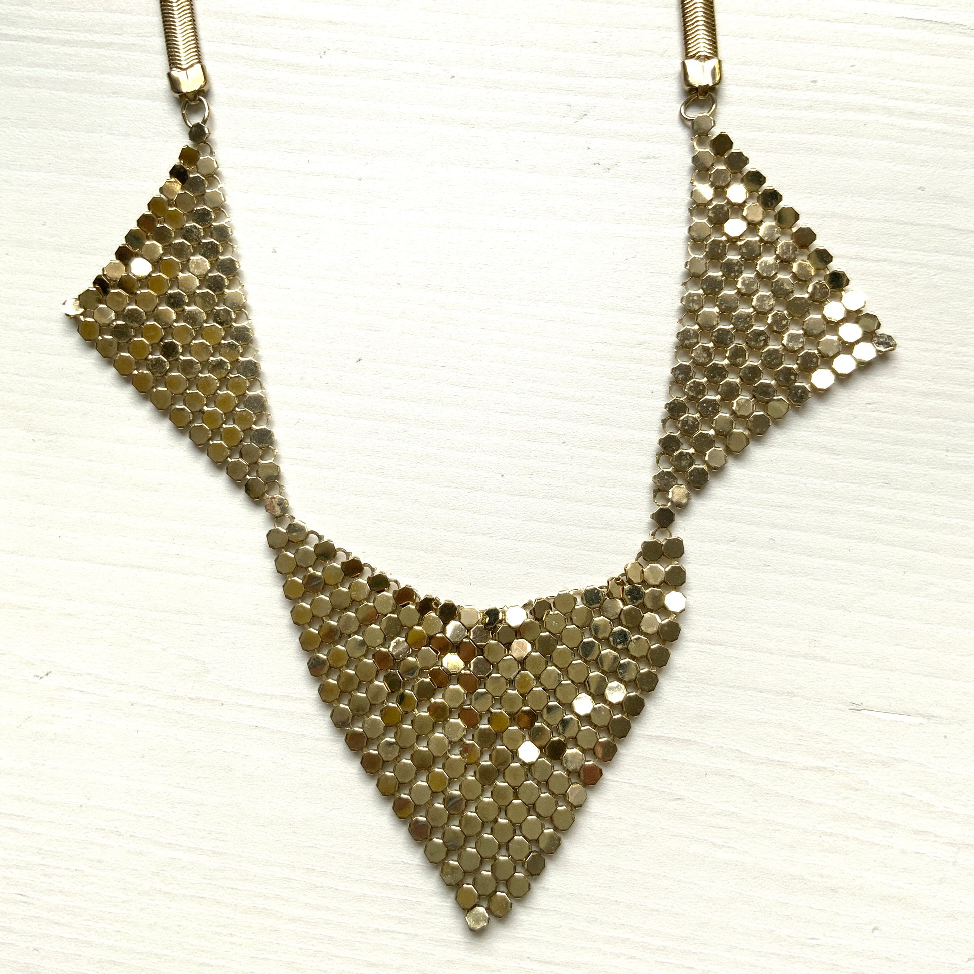 Gold-tone necklace featuring a combination of triangular metal mesh panels. 三角形のメタルメッシュを組み合わせた、ゴールドトーンのネックレス。