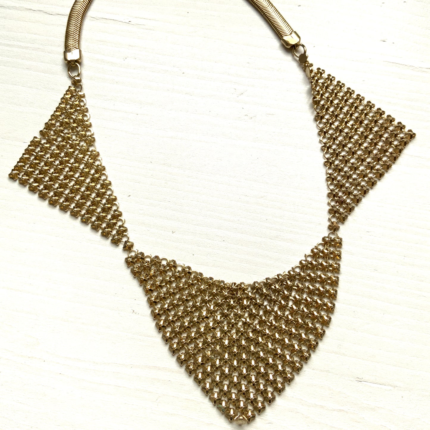 Gold-tone necklace featuring a combination of triangular metal mesh panels. 三角形のメタルメッシュを組み合わせた、ゴールドトーンのネックレス。