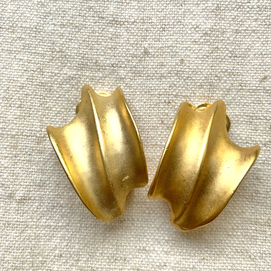 Matte gold-tone clip-on earrings with a simple abstract form. シンプルな抽象的フォルムが印象的な、マットゴールドトーンのクリップイヤリング。