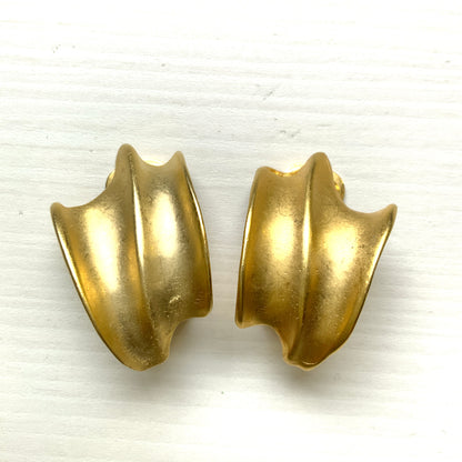 Matte gold-tone clip-on earrings with a simple abstract form. シンプルな抽象的フォルムが印象的な、マットゴールドトーンのクリップイヤリング。